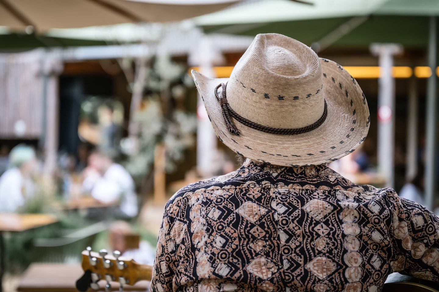 back of man's head, wearing cowboy hat and playing guitar in bath house cafe