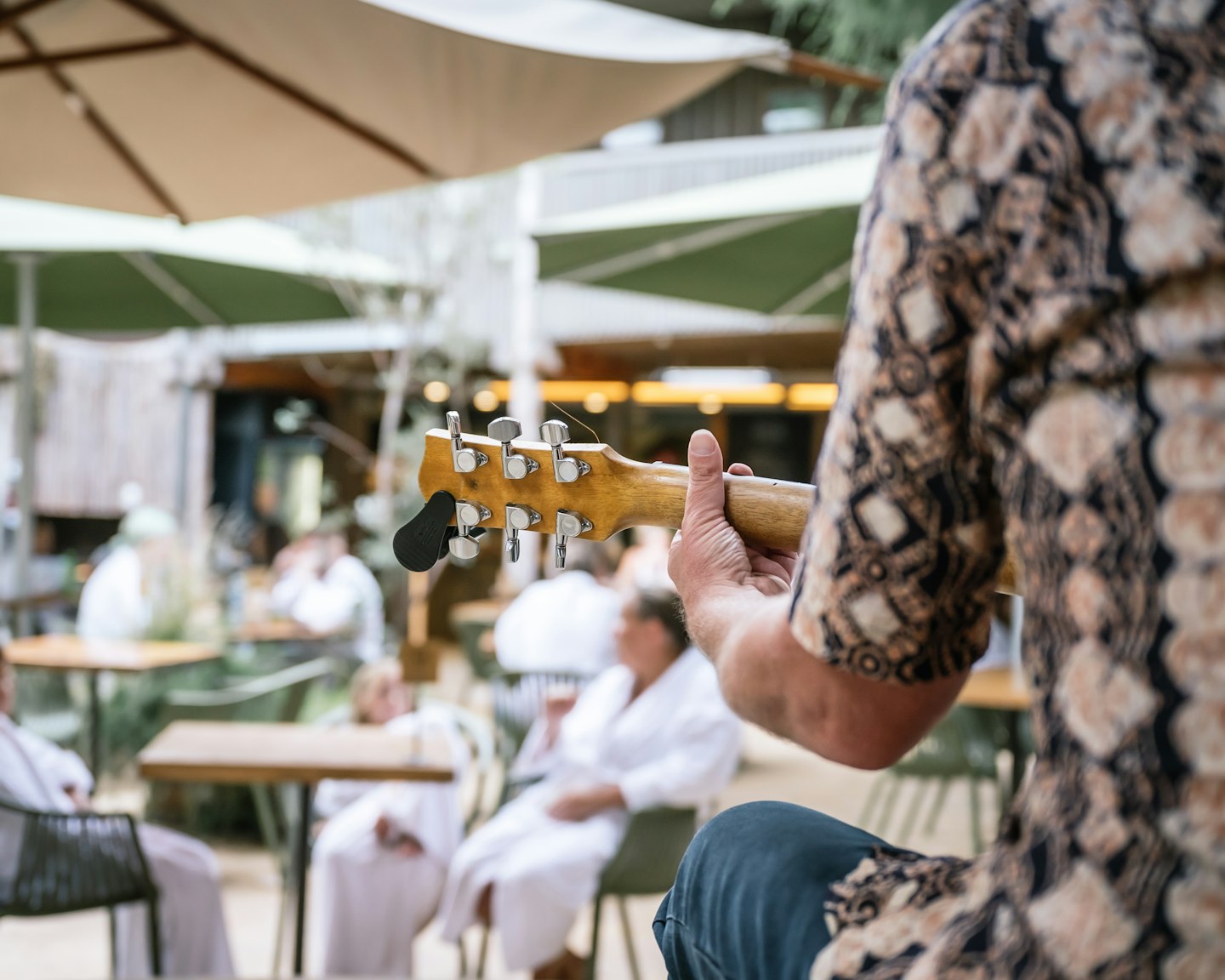 back view of man playing guitar with people in background in white bath robes sitting at café tables