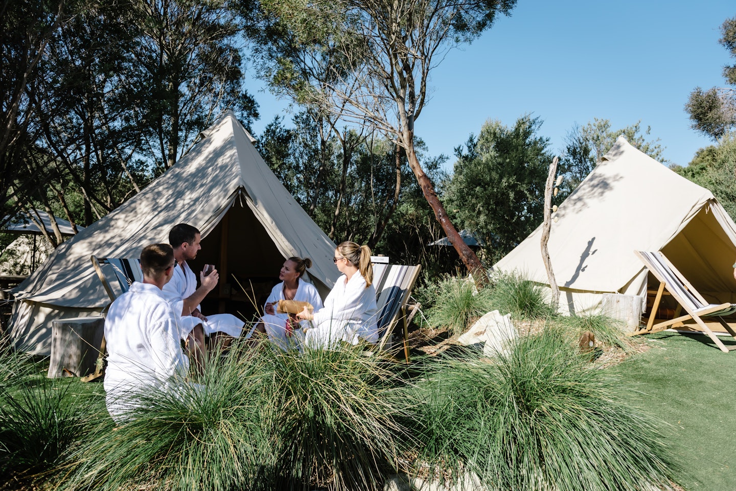 group of four friends in white bath robes sitting on deck chairs outside a relaxation cabana