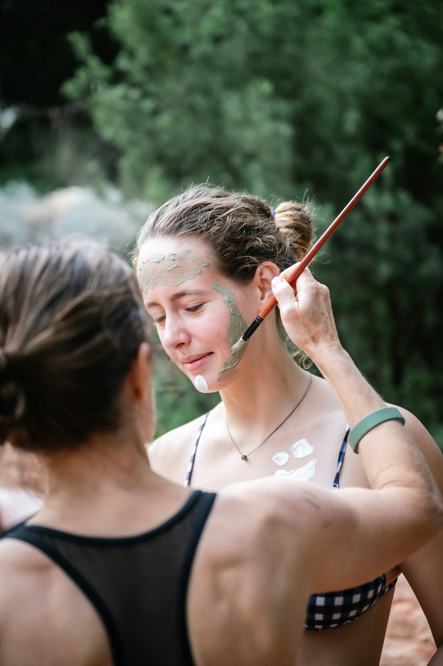 Lady painting girl's face with body clay