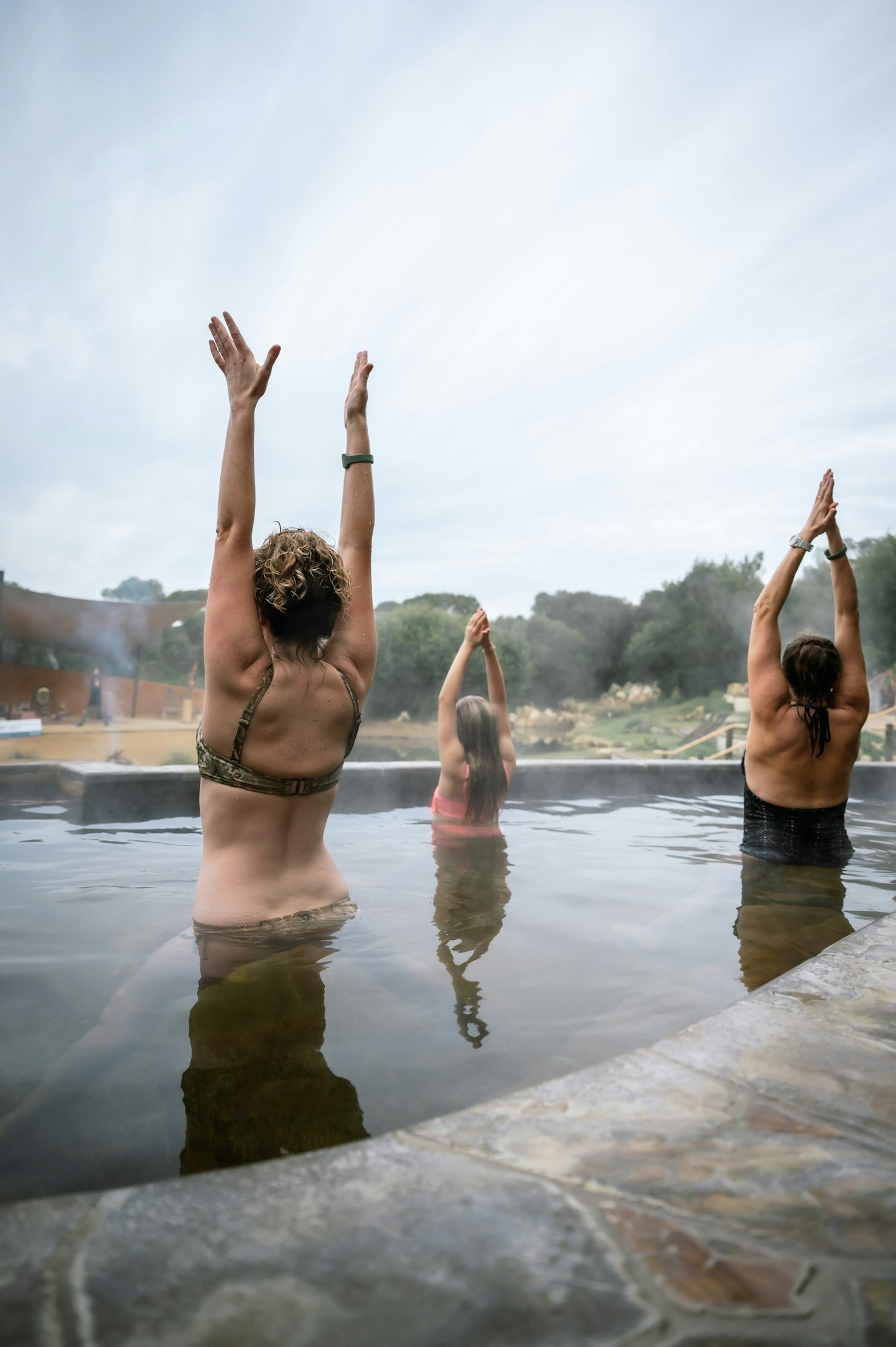 Three ladies in hot springs pool doing sun salutation yoga pose