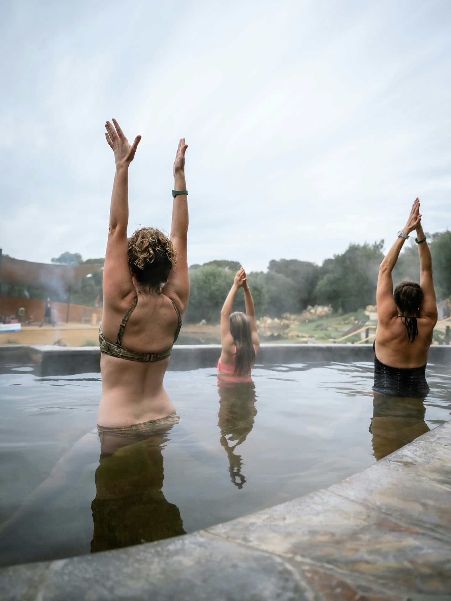 Three ladies in hot springs pool doing sun salutation yoga pose