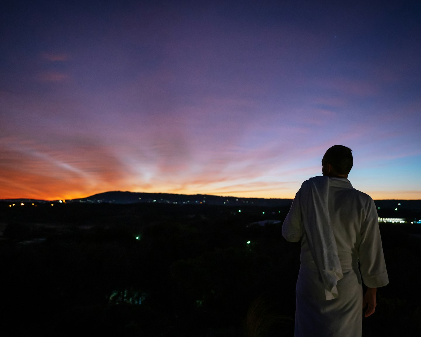 man in white bath robe standing on hilltop looking out at sun about to rise
