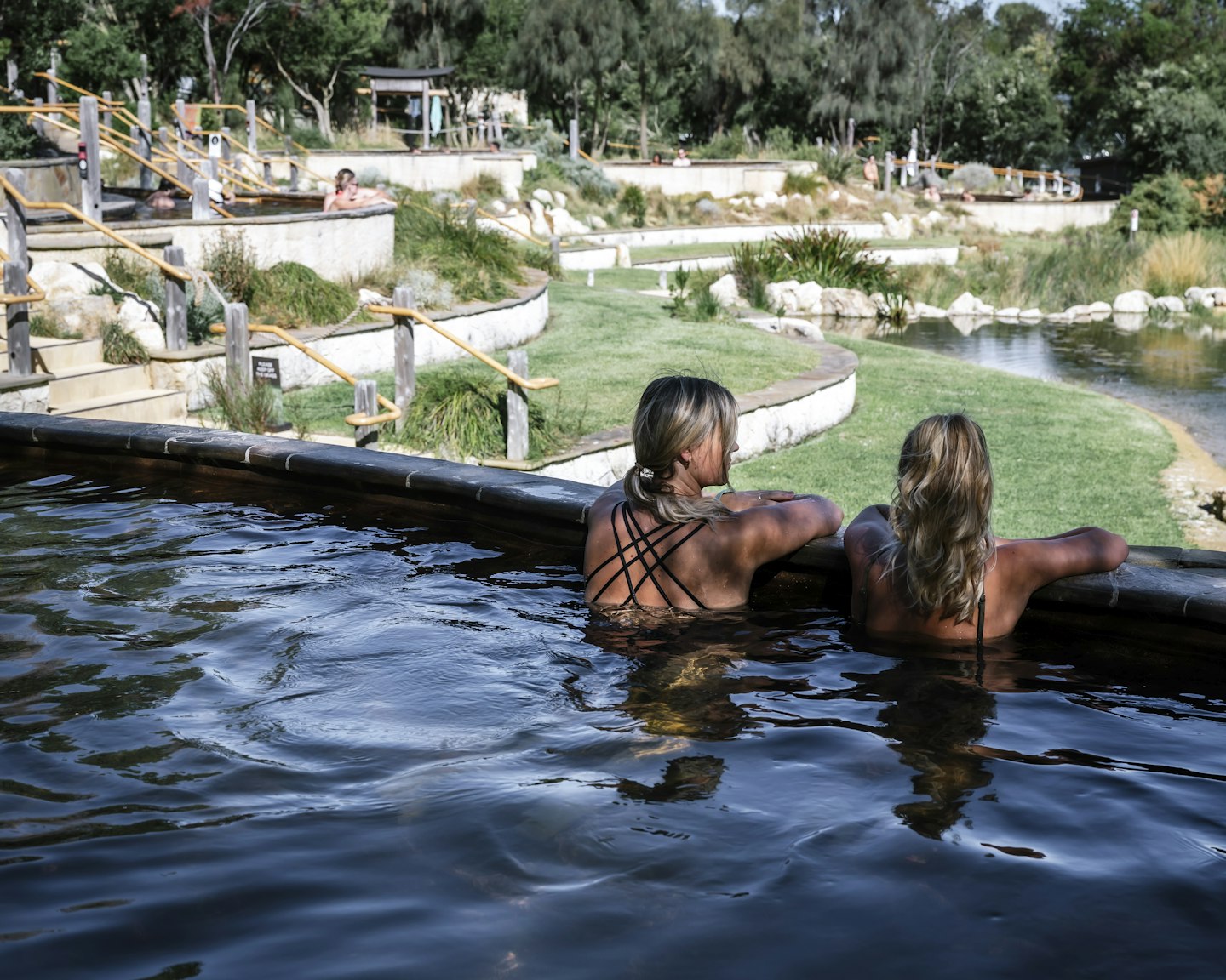 Backs of two girls sitting in geothermal pool looking out over view of nature