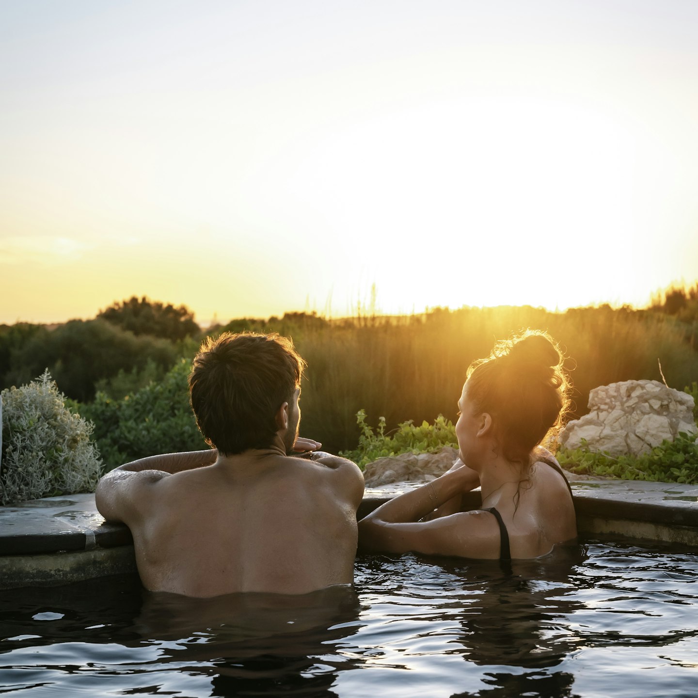 man and woman in geothermal pool looking out at nature and sunset