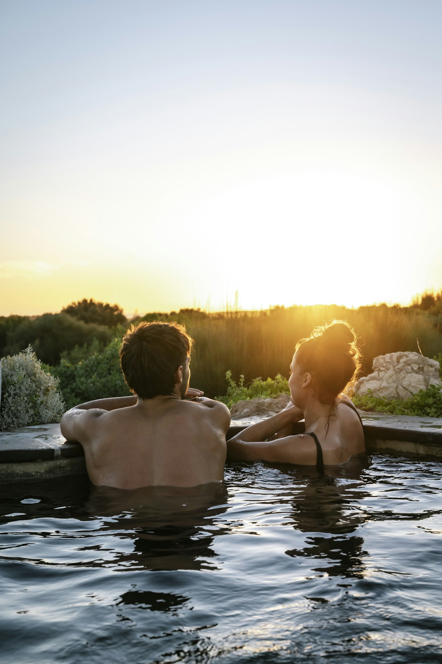 man and woman in geothermal pool looking out at nature and sunset