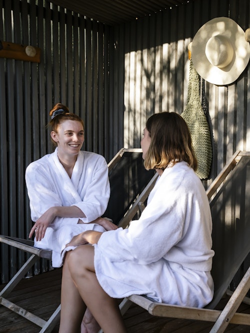 two ladies in white bathrobes sitting on deck chairs chatting
