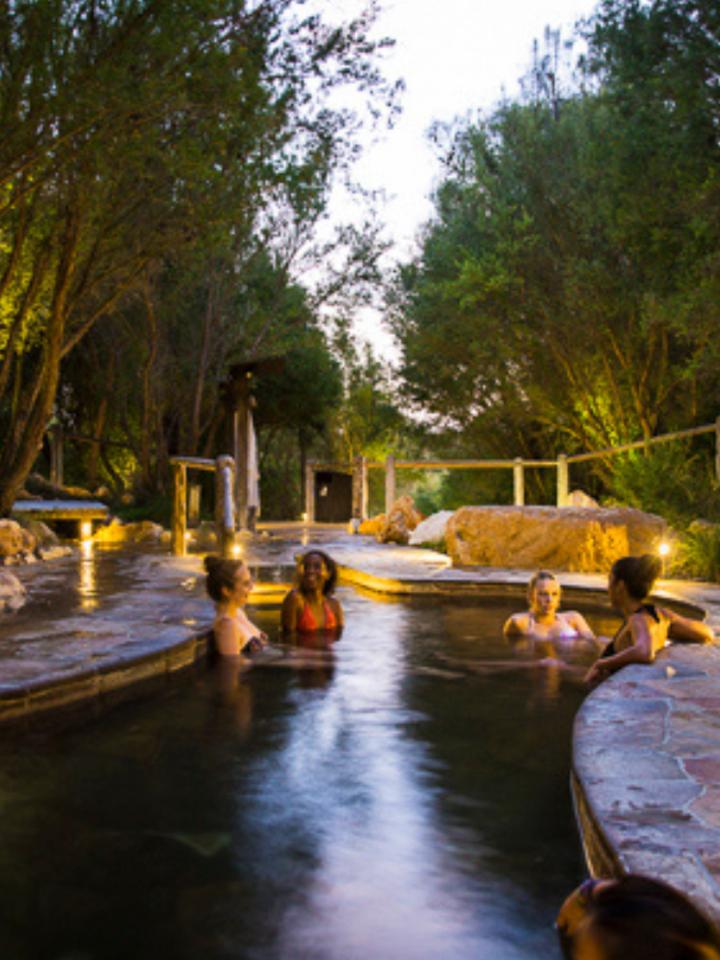 Four young ladies in bathing suits relaxing in geothermal pool at twilight