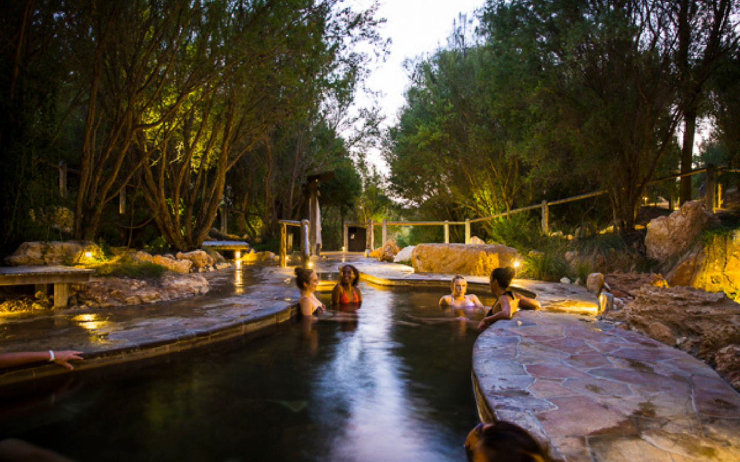 Four young ladies in bathing suits relaxing in geothermal pool at twilight