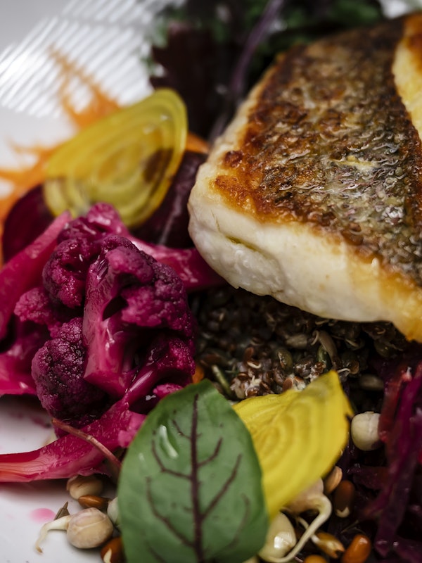 piece of fish sitting on a bed of beetroot, quinoa and garnished with beetroot leaves