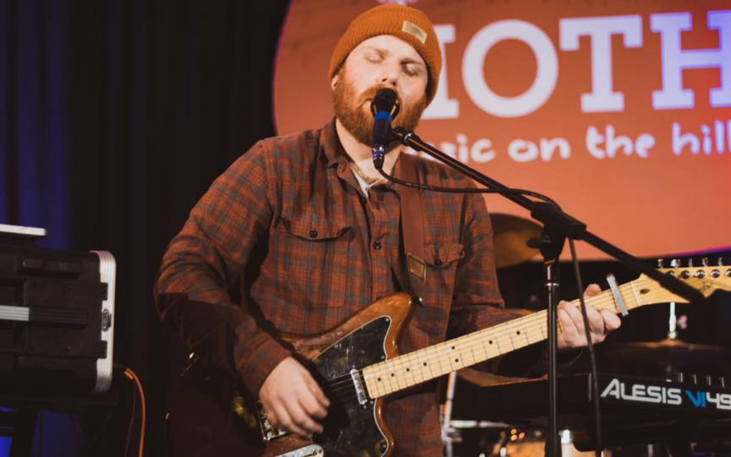 man on stage playing guitar and singing into microphone with eyes closed