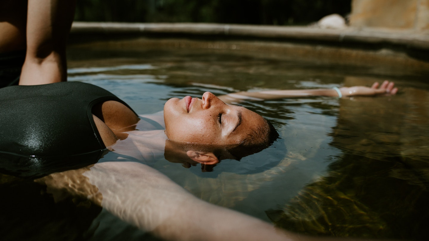 woman floating on her back with her eyes closed in geothermal pool