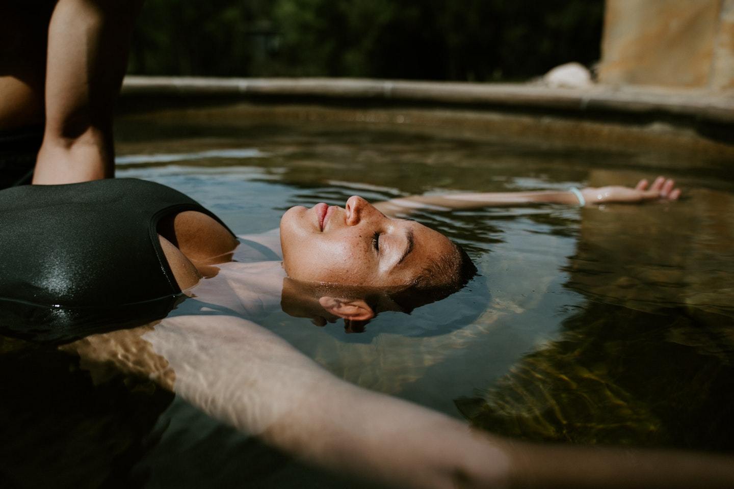 woman floating on her back with her eyes closed in geothermal pool