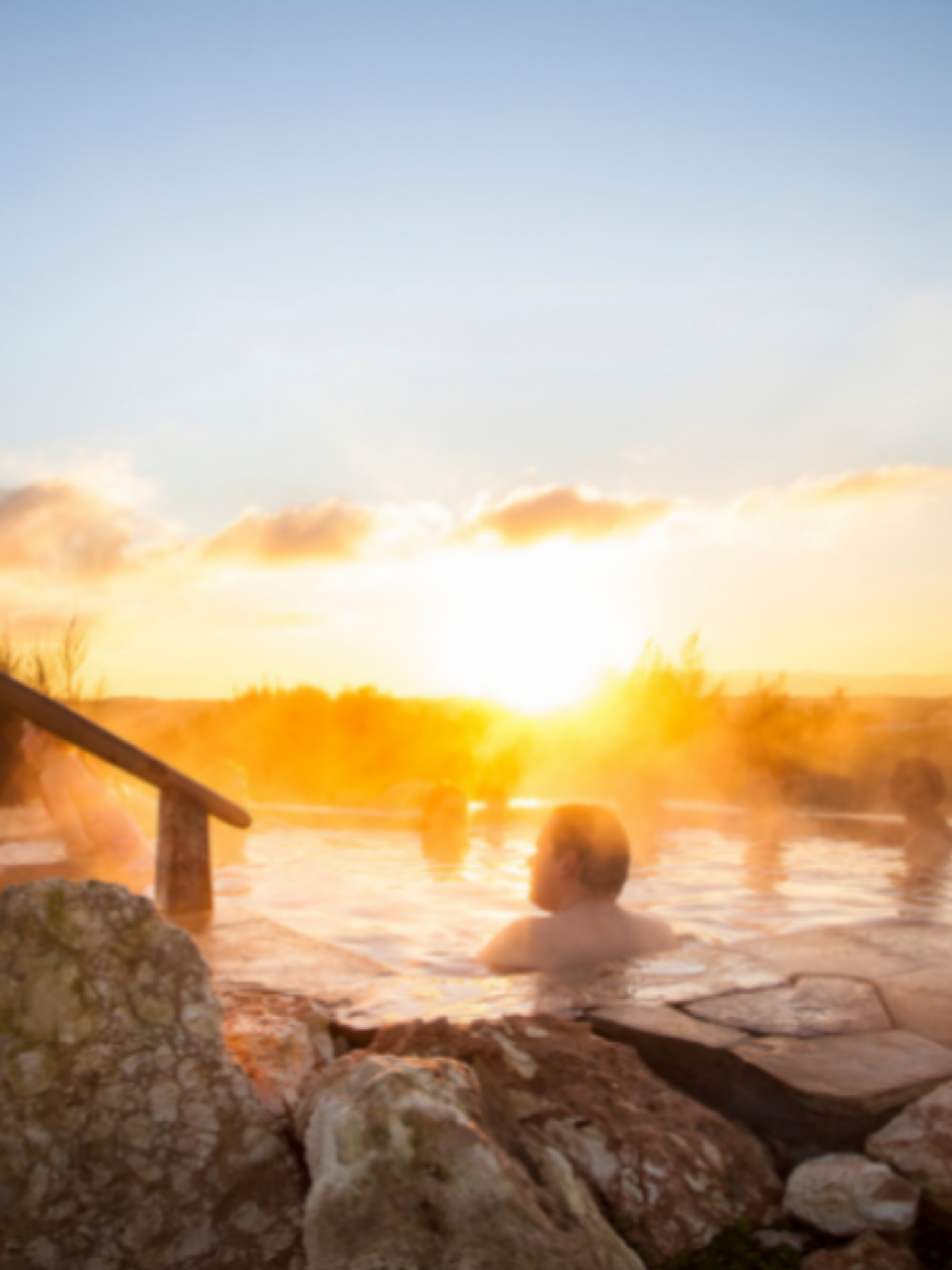 people sitting in steamy hilltop geothermal pool with sun rising