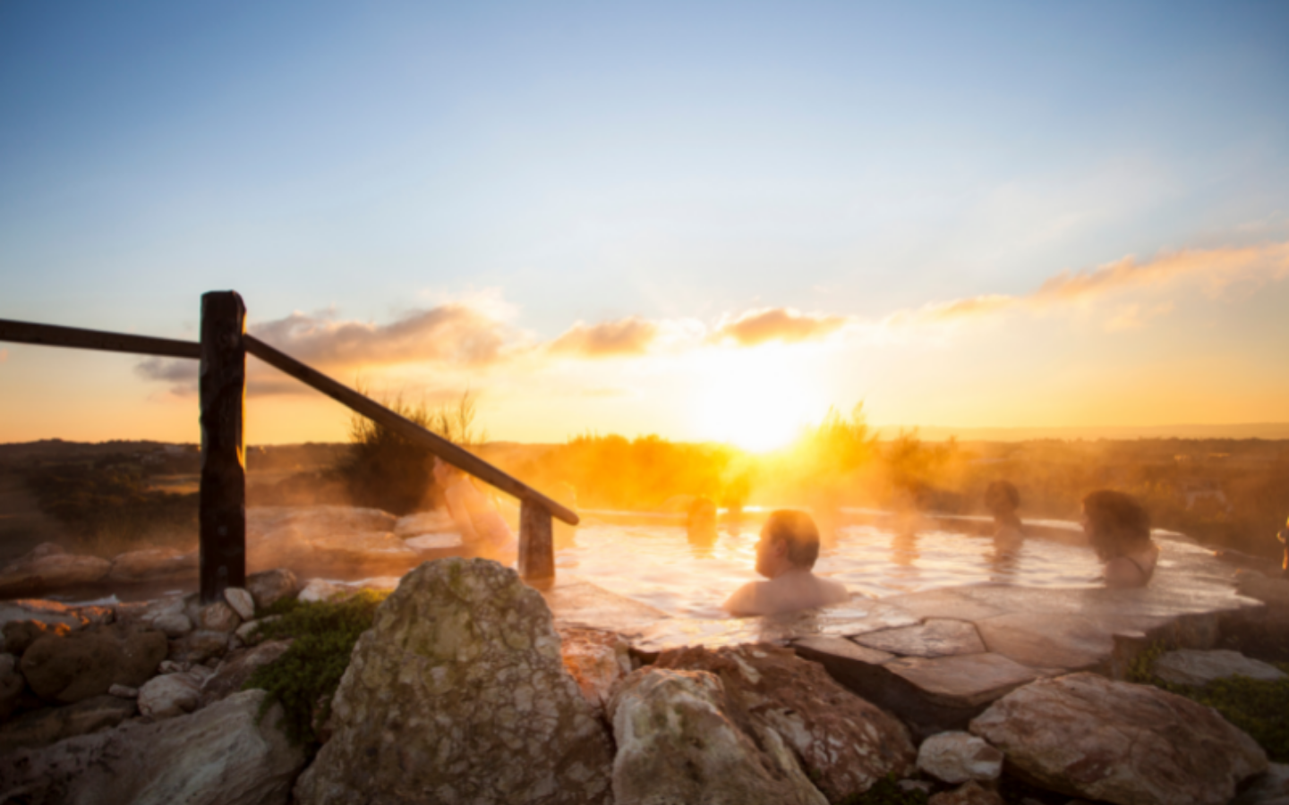 people sitting in steamy hilltop geothermal pool with sun rising