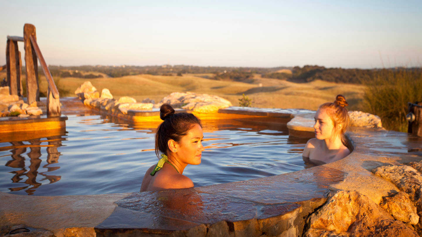 two women sitting in hilltop geothermal pool looking out at view
