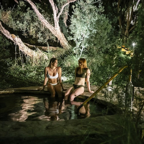 two ladies sitting on edge of geothermal pool moonlit bathing at night time