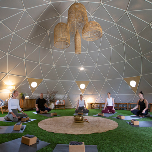 group sitting in yoga pose in semi circle in geodesic dome