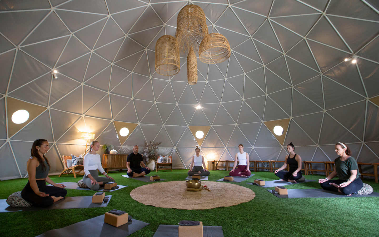 group sitting in yoga pose in semi circle in geodesic dome