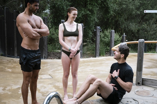 Instructor sitting beside cold pool teaching a man and a woman in bathing suits about hot cold therapy