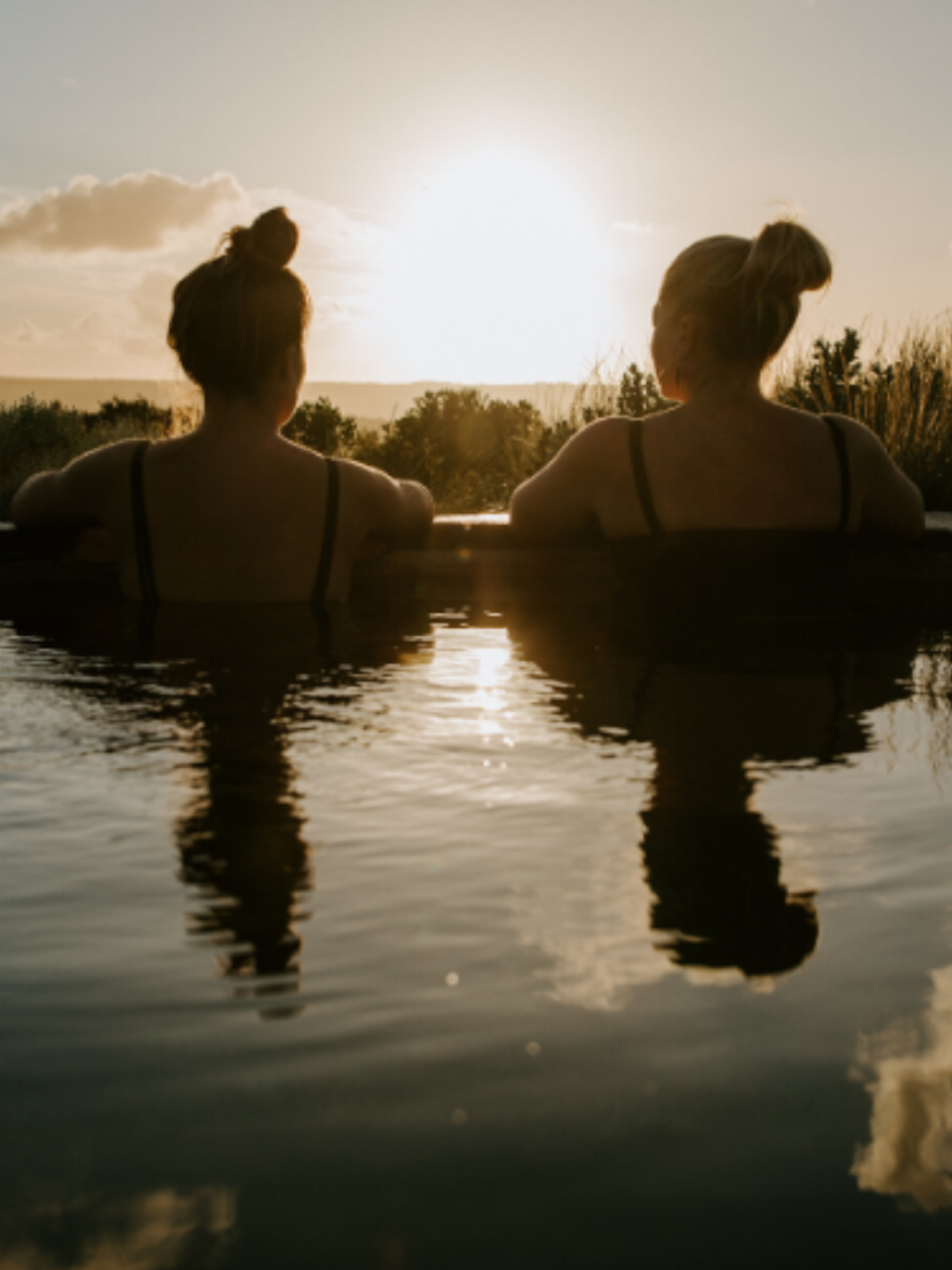 two women sitting in hilltop pool as the sun rises