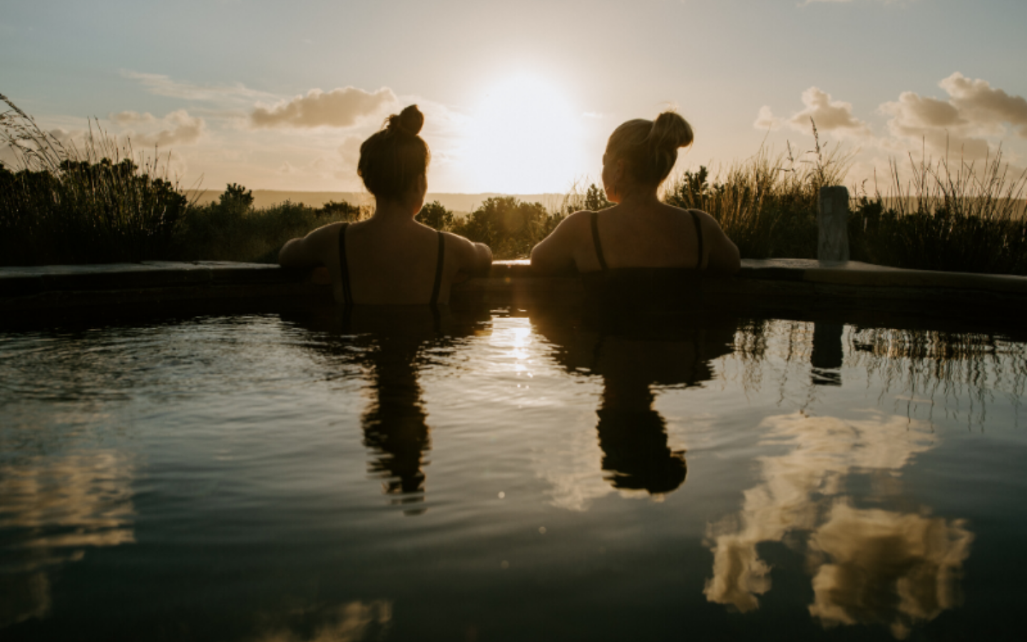 two women sitting in hilltop pool as the sun rises