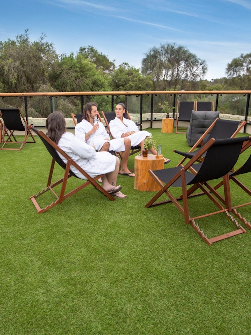 three people sitting on deck chairs on expansive, grassed sun lounge
