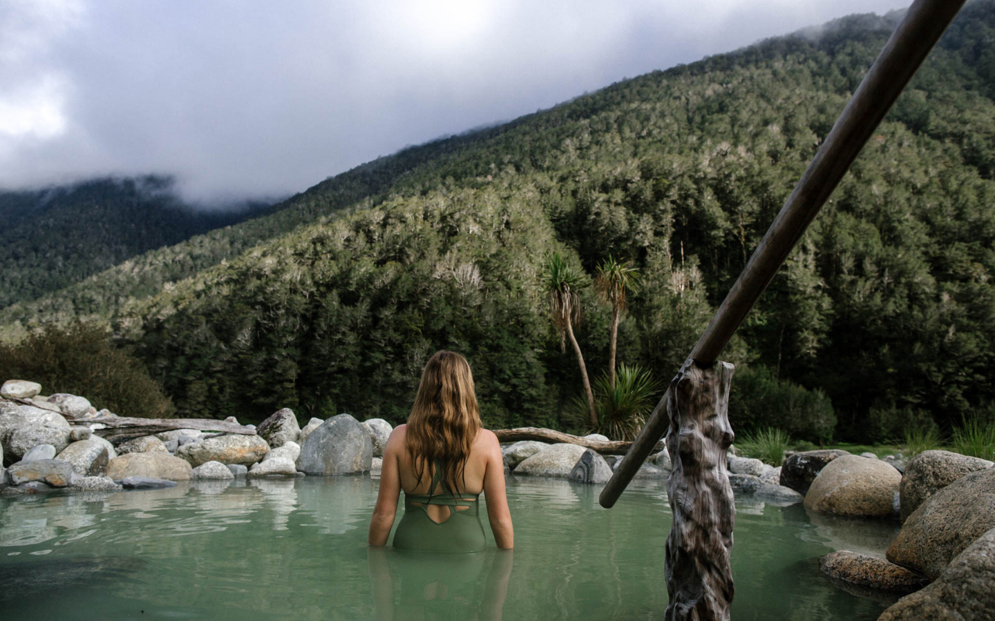 woman in bathing suit standing in geothermal pool looking out at mountain forrest