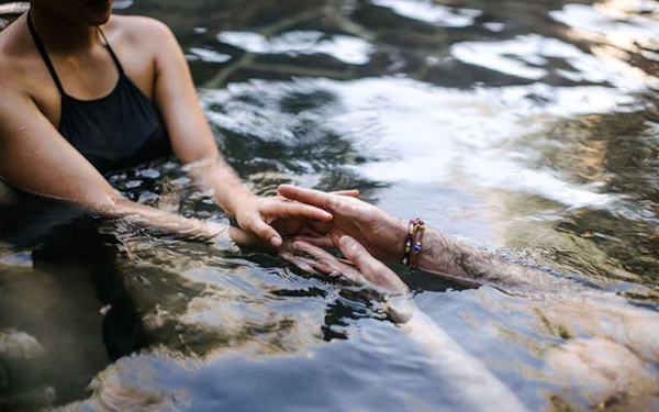 man and woman holding outstretched hands in geothermal waters