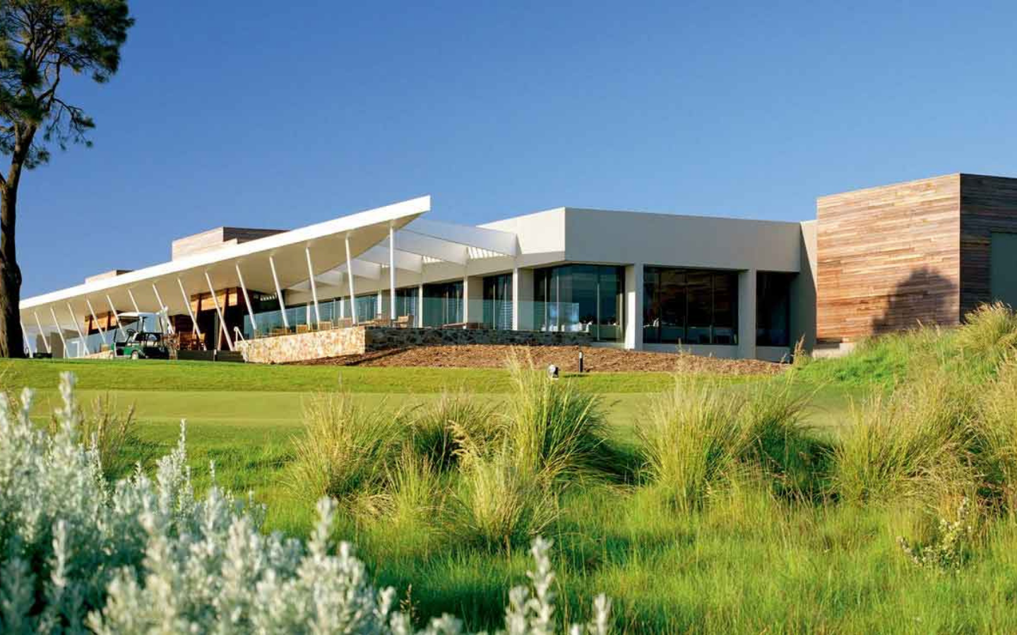 view of architectural building, grasses in the foreground, golf buggies in the background