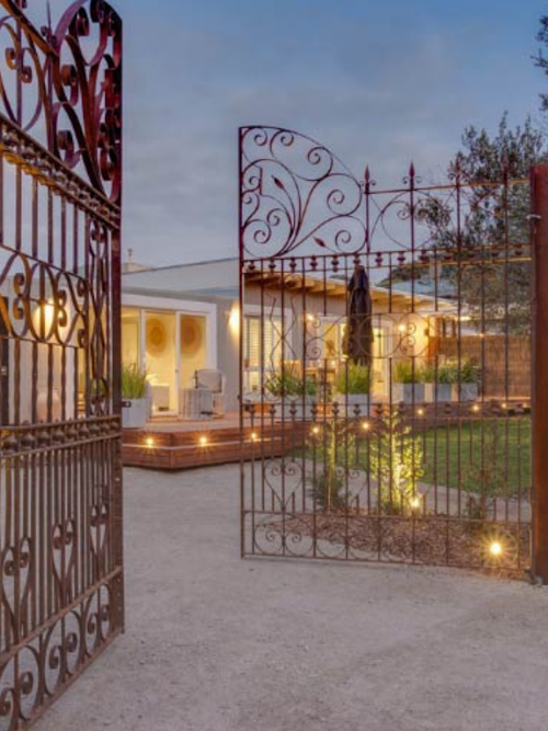wrought iron gates open to lit up home and garden