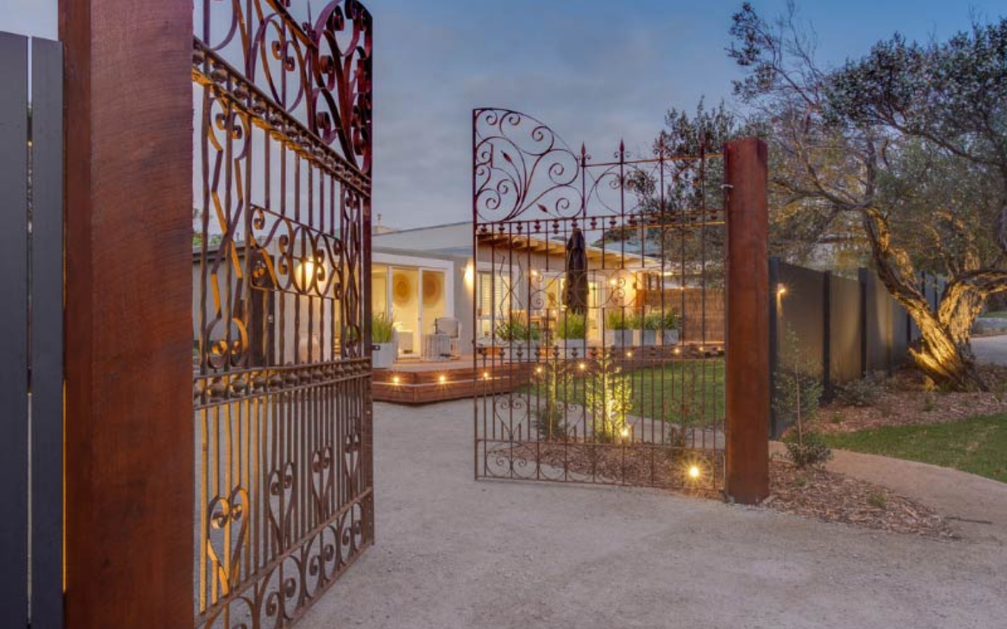 wrought iron gates open to lit up home and garden