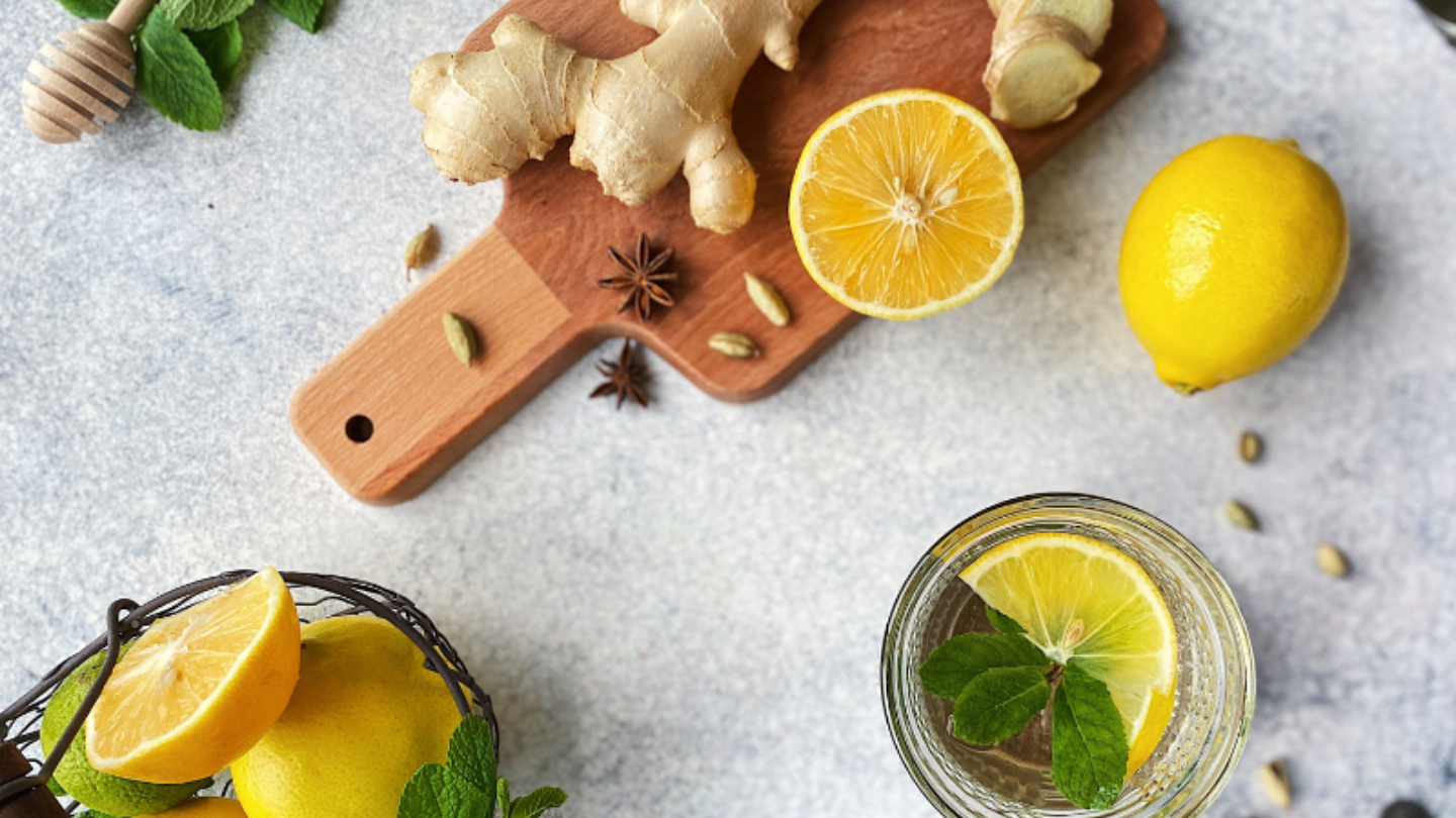 lemon and ginger sitting on a wooden board with a drink with lemon, ginger and mint to the side