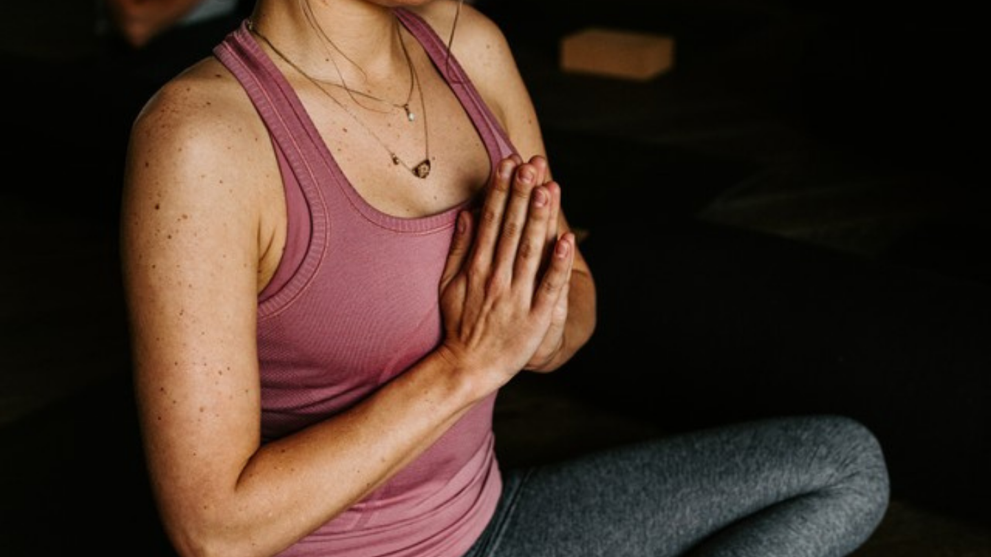 woman with hands in prayer sitting cross legged