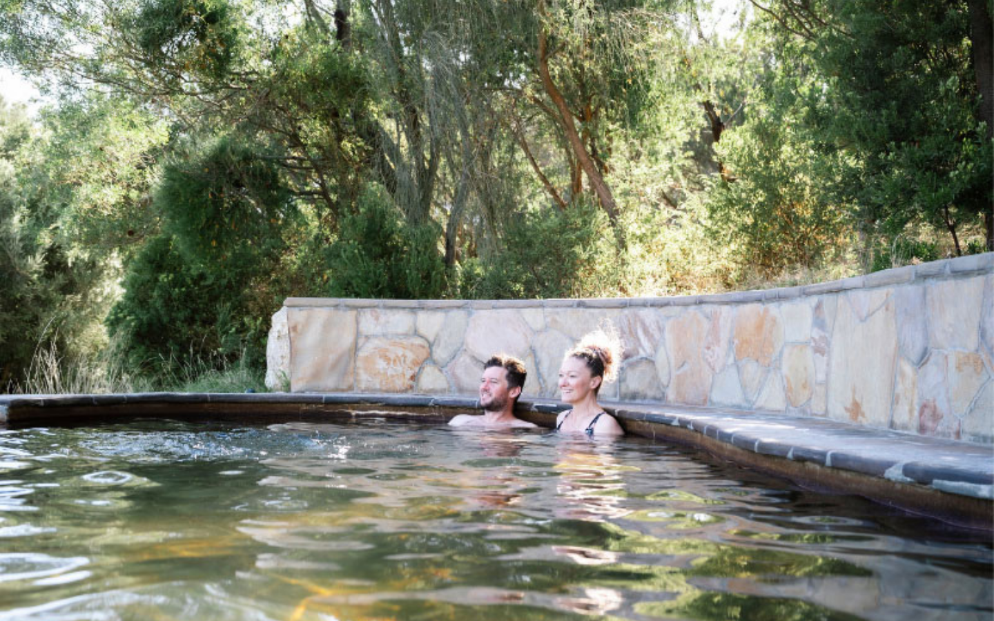 a man and woman sitting in a hot pool looking outward