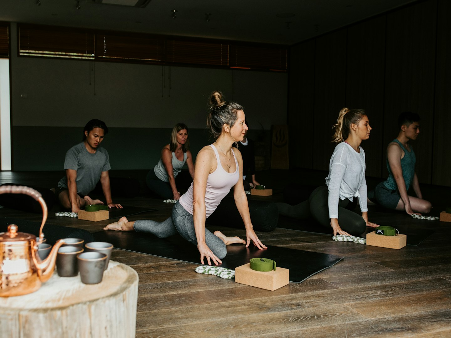 group of six people doing yoga stretches on mats on wooden floor