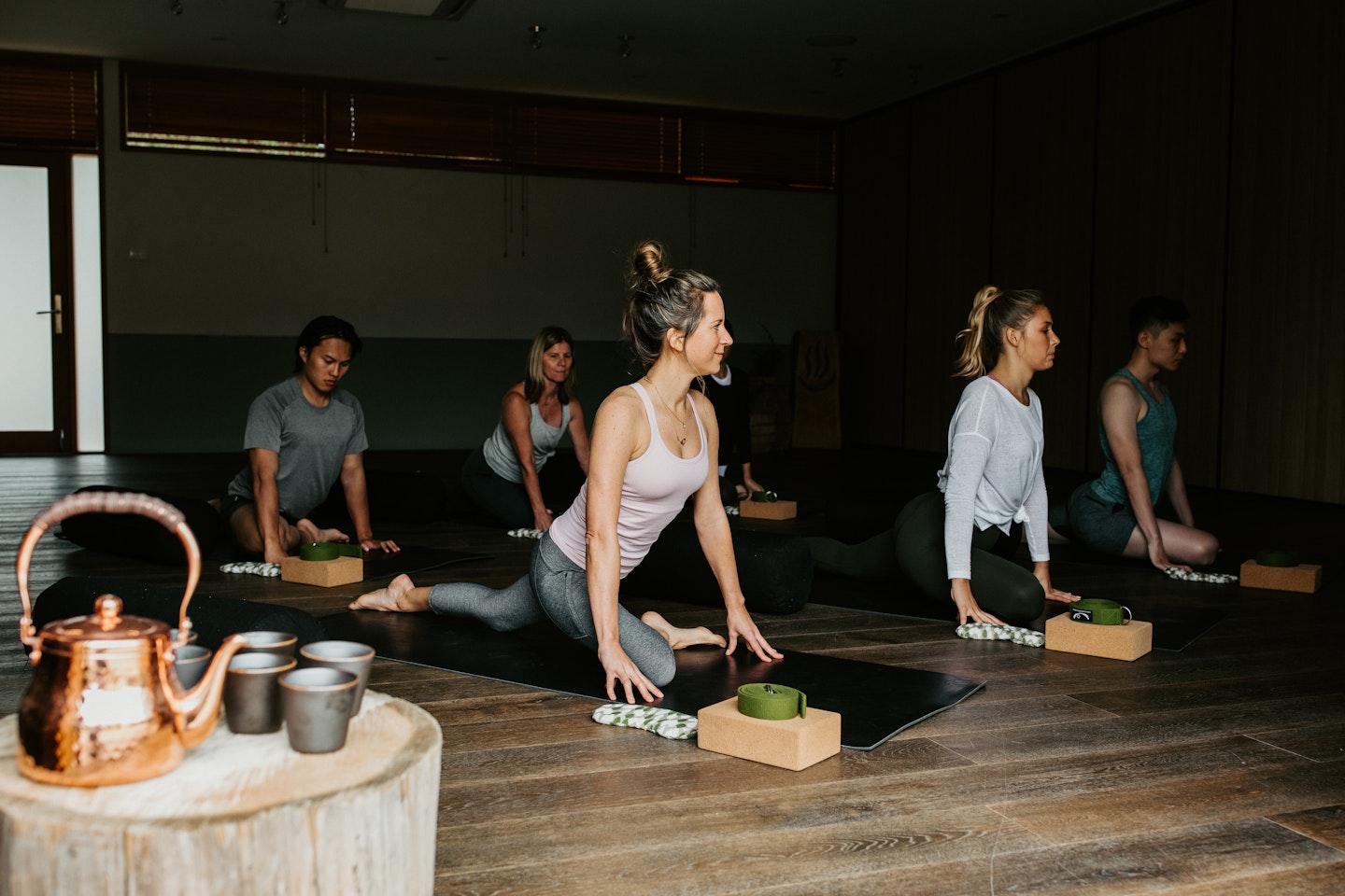 group of six people doing yoga stretches on mats on wooden floor