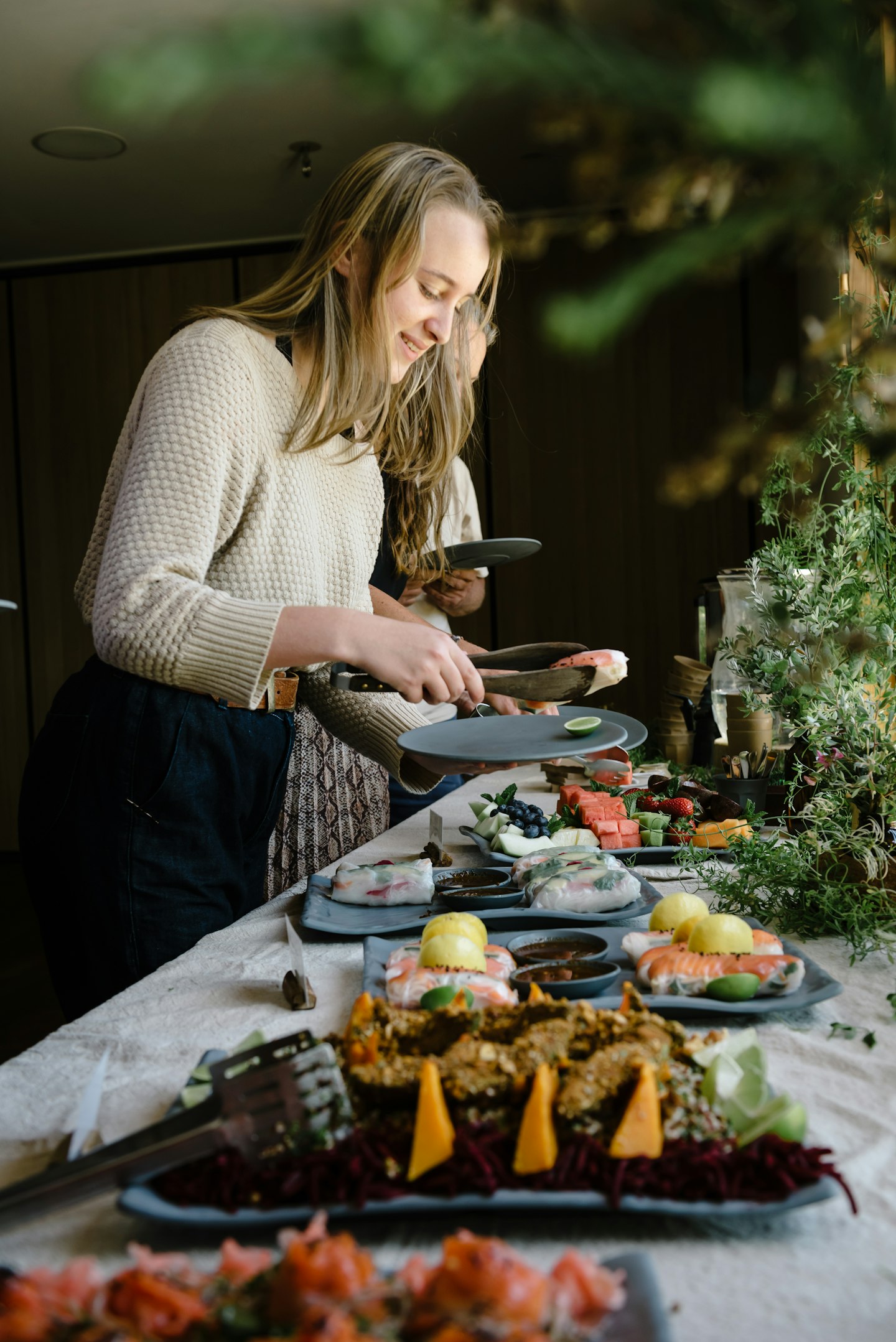 table with buffet style lunch laid out and woman putting food on her plate