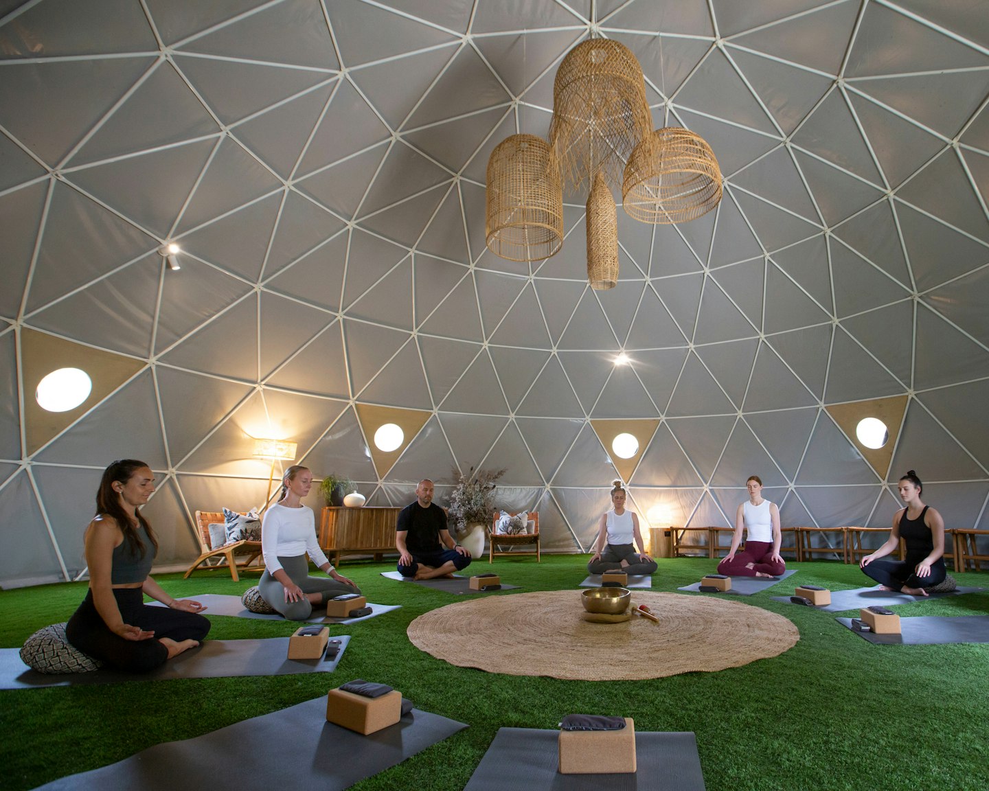 group of seven people sitting in a circle on yoga mats inside a geodesic dome 