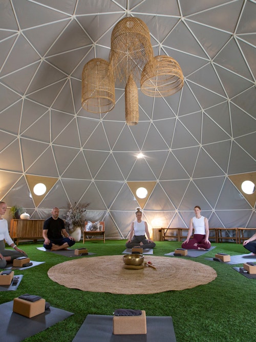 group of seven people sitting in a circle on yoga mats inside a geodesic dome 
