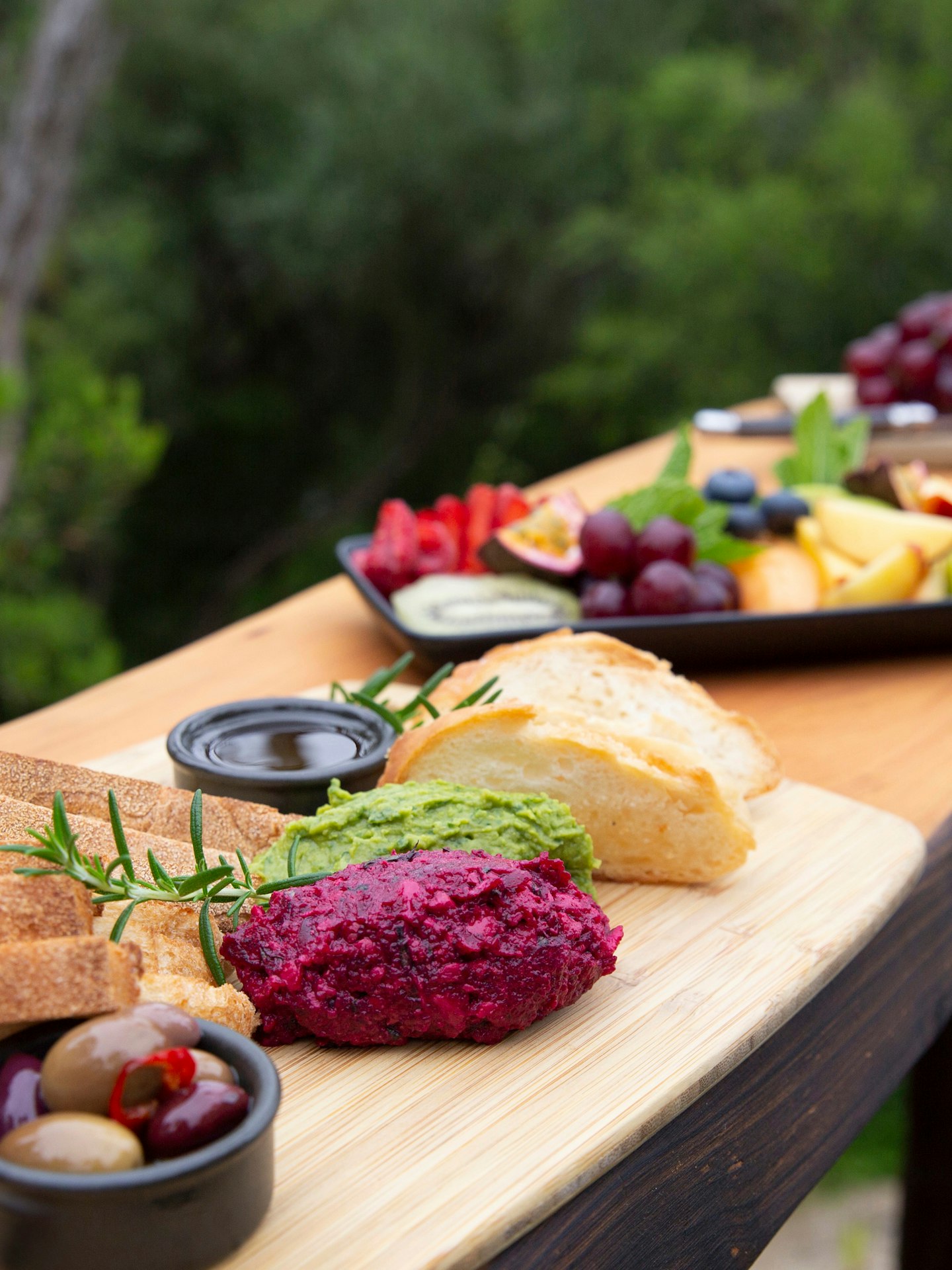 beautiful, colourful platters of food laid out on elevated wooden ledge with trees in background
