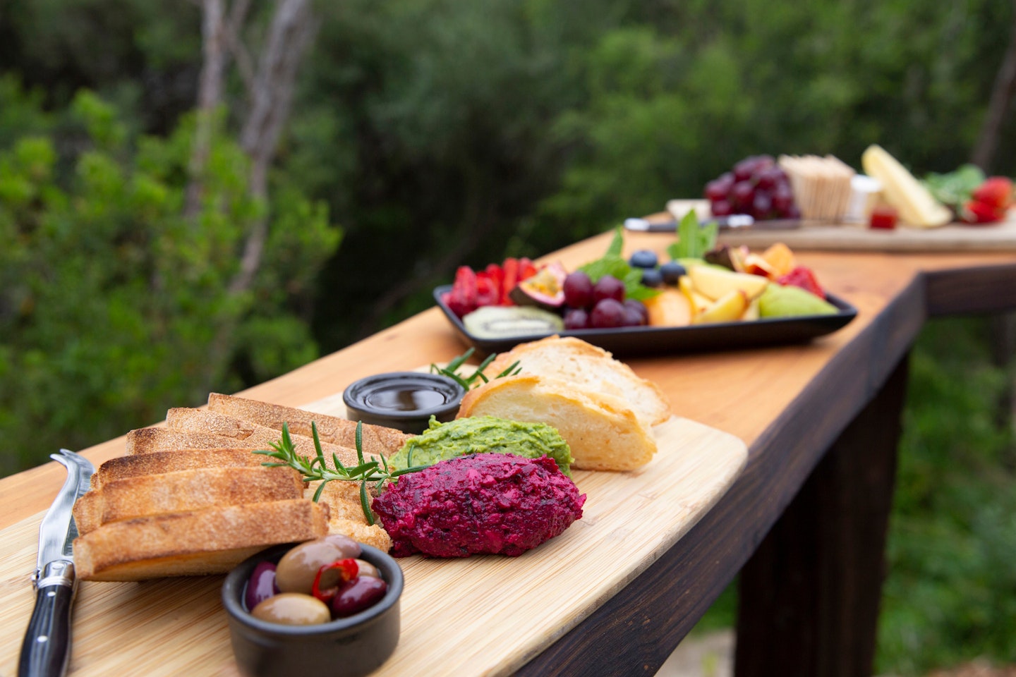 beautiful, colourful platters of food laid out on elevated wooden ledge with trees in background