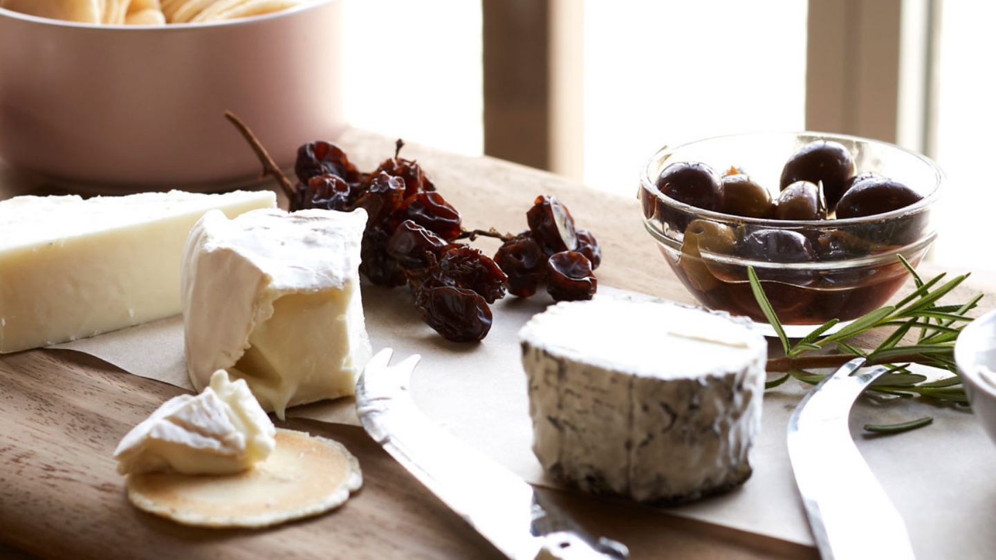 a selection of cheeses lined up on a wooden board with olives