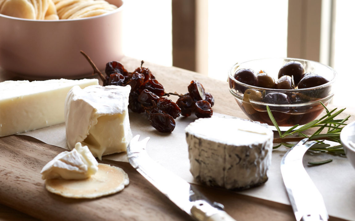 a selection of cheeses lined up on a wooden board with olives