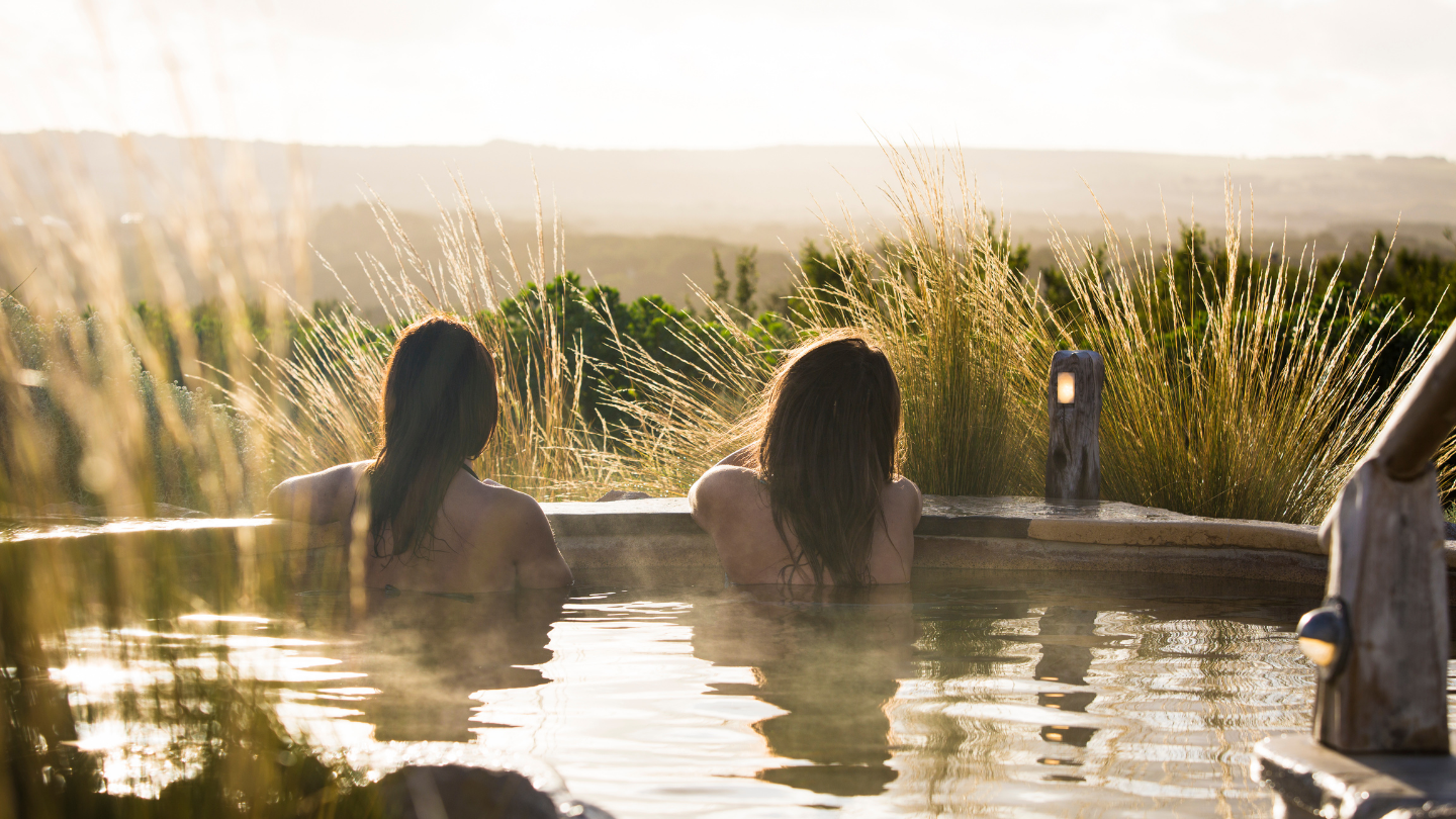 two women relaxing in hilltop pool looking out at view