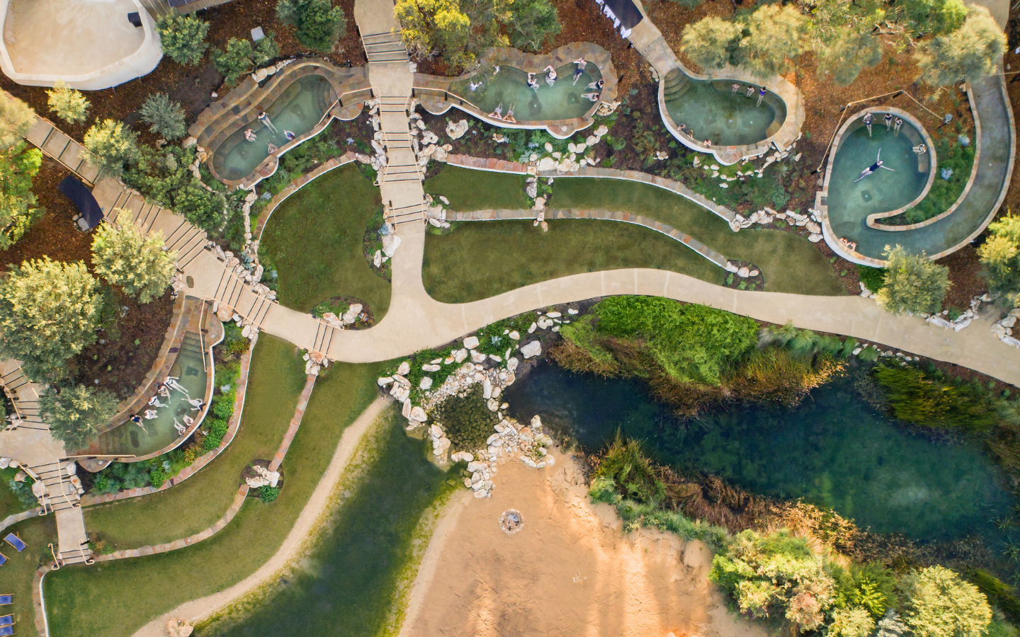 aerial view of bath house amphitheatre with people bathing in curved pools set into the landscape with winding paths and nature all around