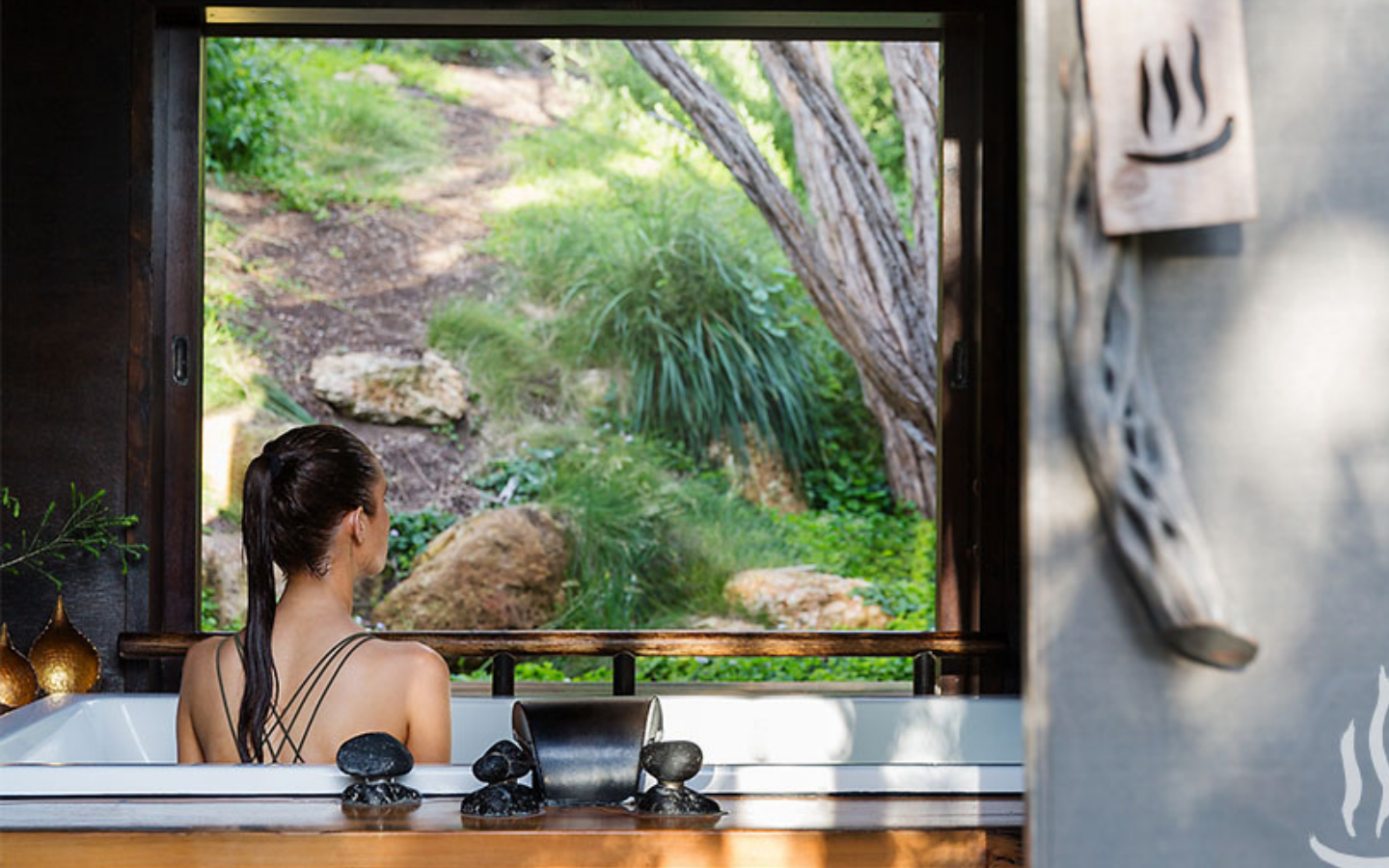 view of back of woman with long ponytail in bathing suit looking out at nature from her private bath