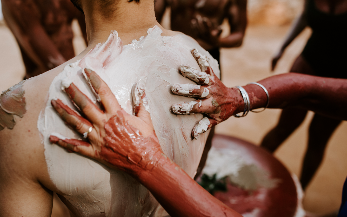 two hands rubbing clay on a person's back