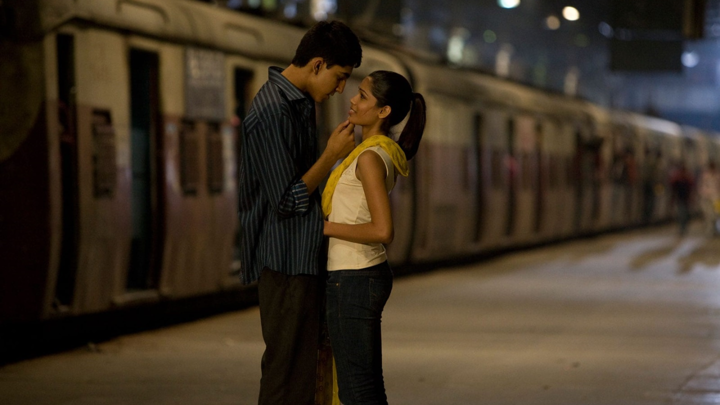 a boy and girl standing in front of a train about to kiss
