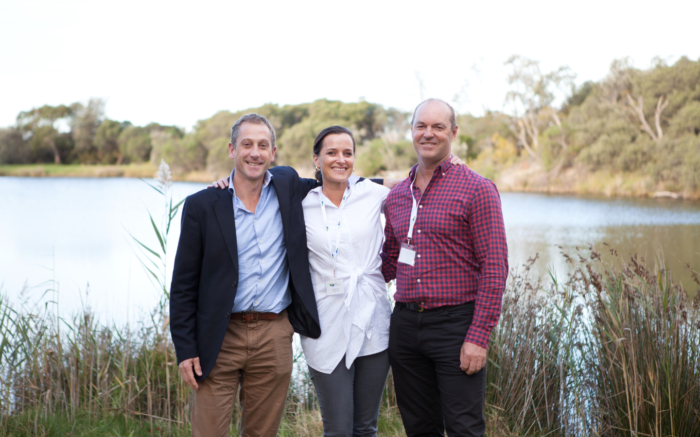 three people standing in front of a lake with their hands around their shoulders